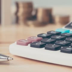 Closeup photo of a calculator sitting on a desk alongside a pen
