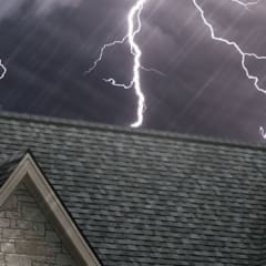 Photo of the top of a roof with gray shingles set against a dark, stormy sky with lightning