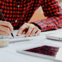 Photo of a person sitting at a desk in front of a laptop taking measurements on a large sheet of paper