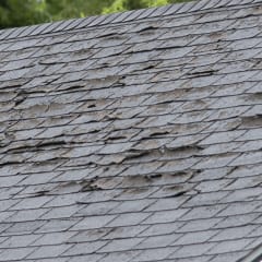 White house with old, grey shingle roof with curing and visible damage