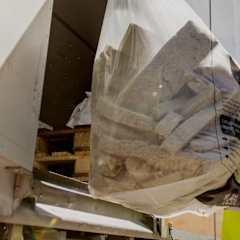 A man dressed in a helmet and high-visibility jacket is loading used stonewool into a truck