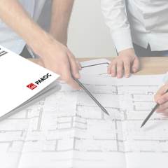 katalogas "statau šiltą namą", gulintis ant stalo kartu su liniuotėmis ir brėžiniais, prie stalo stovi du vyrai ir rodo į brėžinius