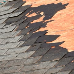 Shingles being torn off a roof showing the wood decking underneath.