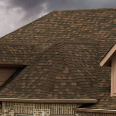 Tan colored house with brown shingles set against a dark, stormy sky with lightning flashing