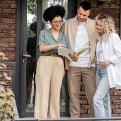 Homebuyers standing in front of brick home reviewing documents with real estate agent,