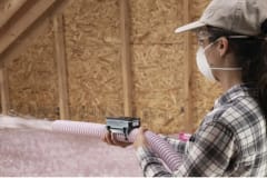 Woman installing AttiCat® blown-in, loose fill insulation covering joists