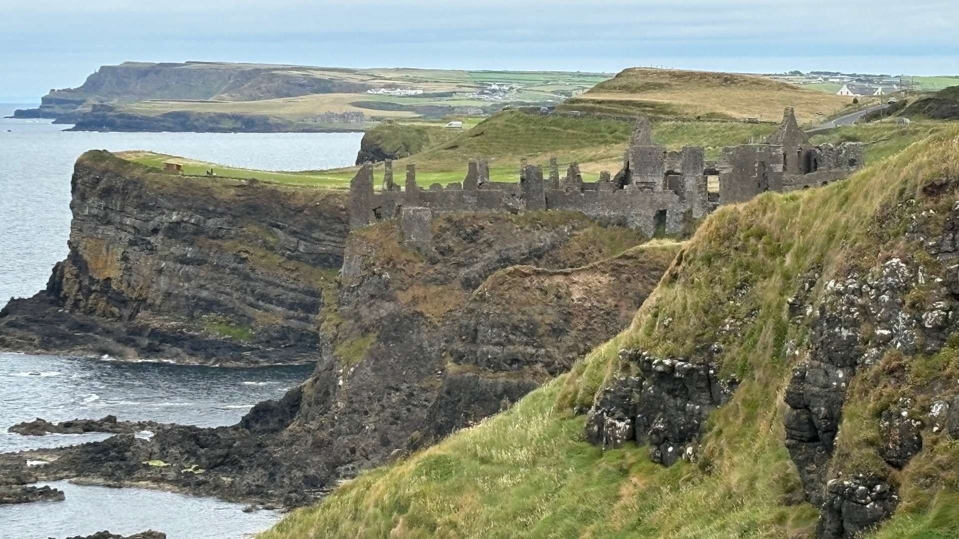 Stone ruins of an ancient castle on rugged sea cliffs overlooking the ocean under a cloudy sky.