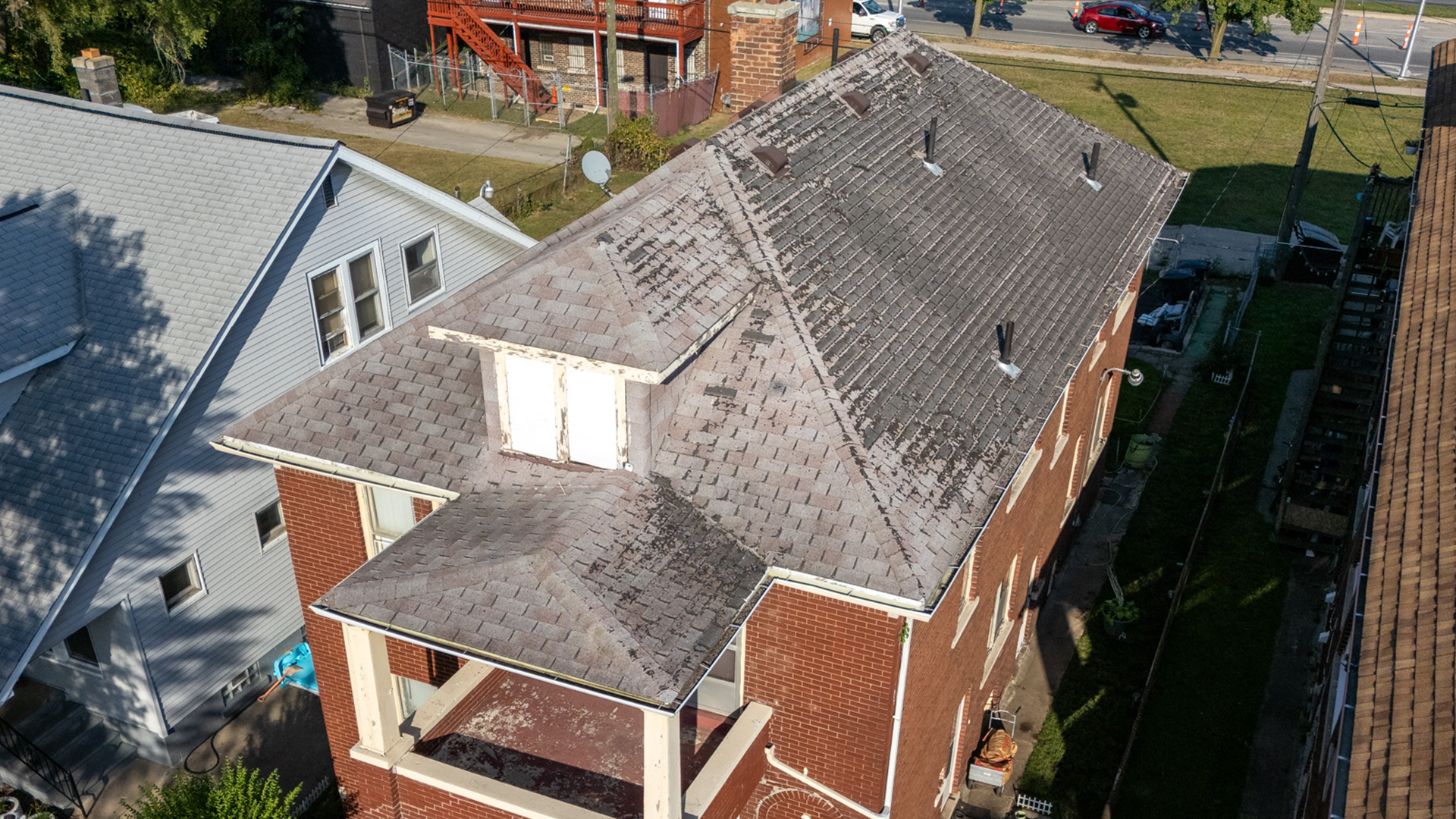 Red-brown bricked multistory home with grey 3tab shingle roof with severe granule loss. 