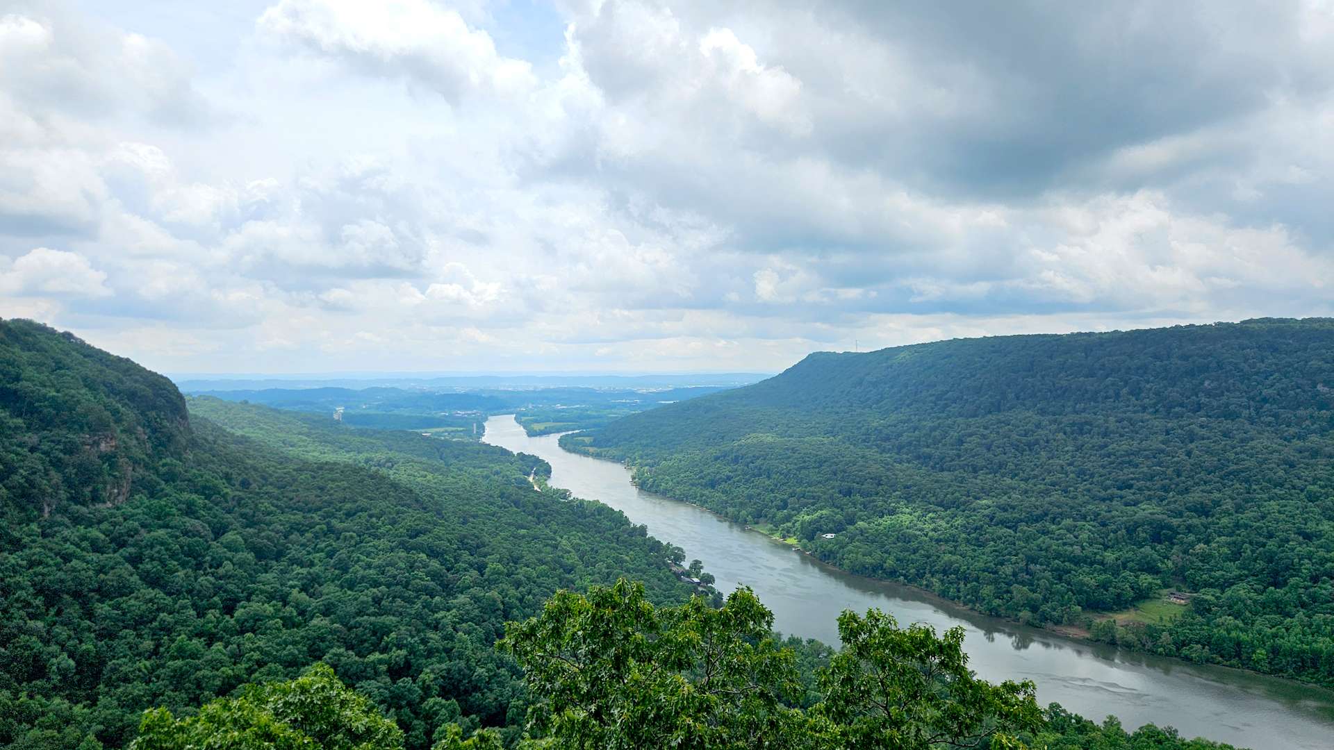 Wide river winding through lush green forested hills under a cloudy sky.