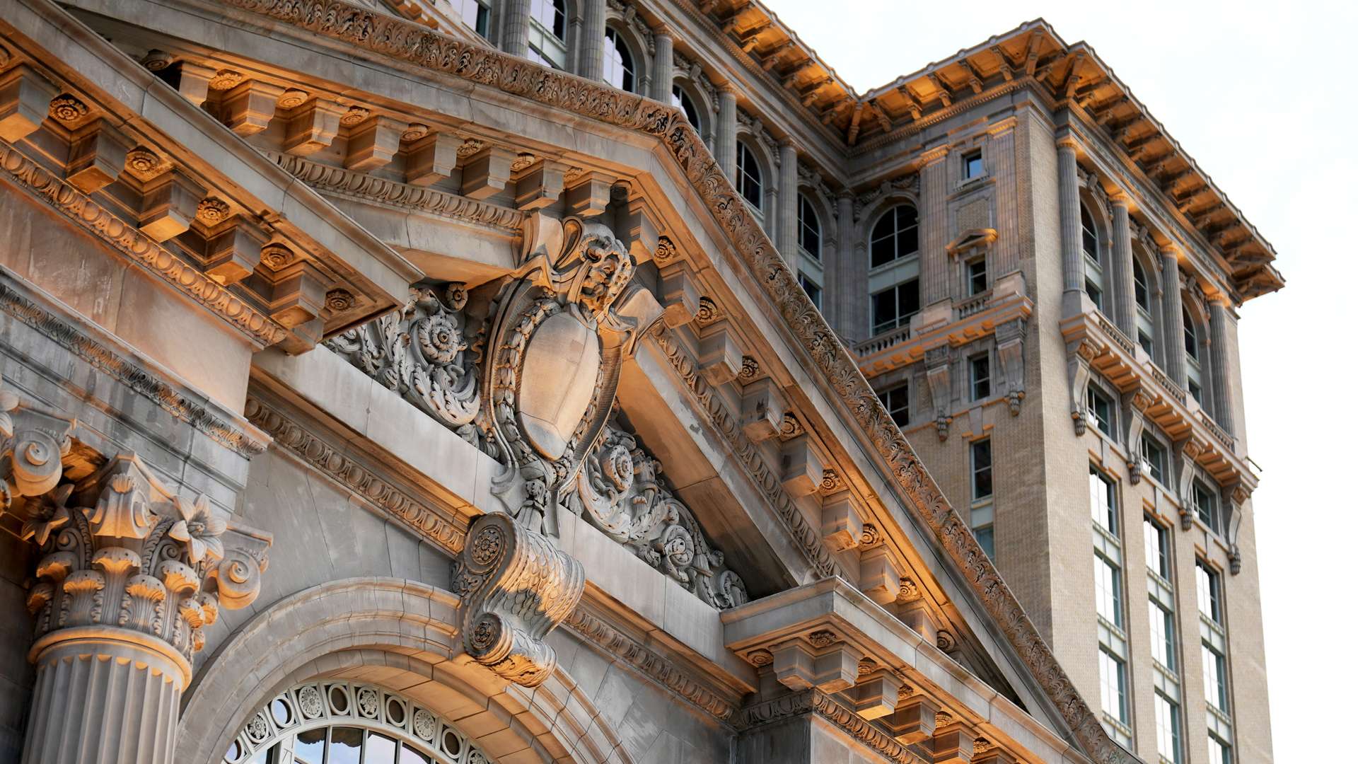   Close-up of ornate historic building facade with detailed stone carvings, columns, and arched windows under soft light.