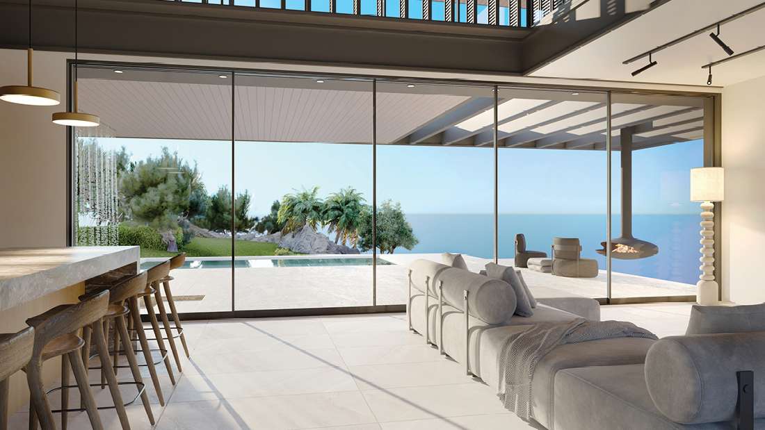 Luxury open-concept living area with floor-to-ceiling glass walls overlooking ocean views, modern sectional sofa, marble kitchen island with wooden bar stools, and contemporary pendant lighting.