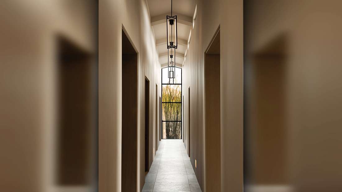 Minimalist hallway with arched ceiling, light beige walls, gray tile flooring, black-framed glass door at the end, and modern rectangular pendant lights.