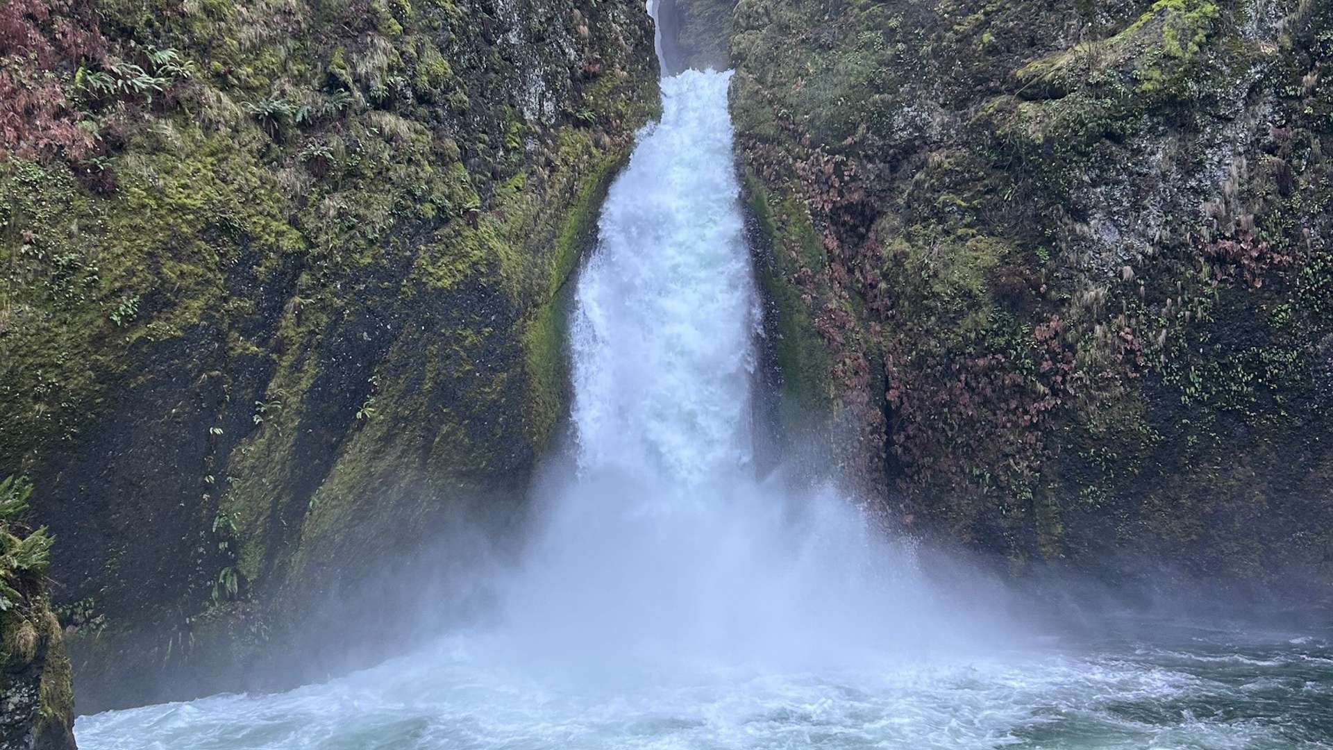   Powerful waterfall cascading between moss-covered rocky cliffs into a swirling pool below.