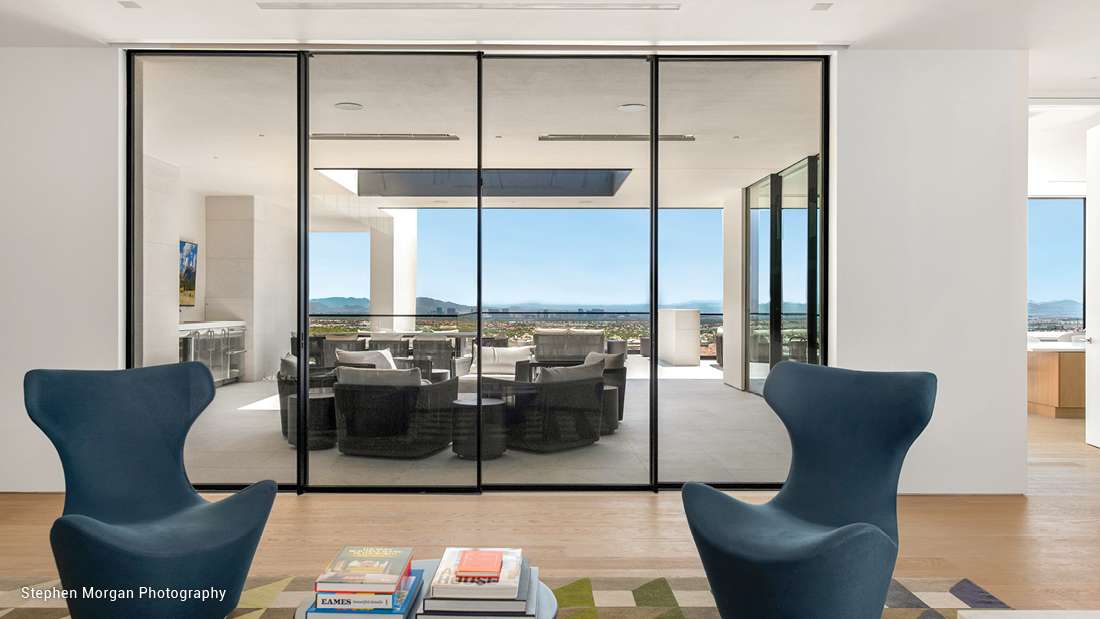 Modern interior with glass sliding doors opening to a spacious terrace, panoramic city and mountain views, and contemporary lounge seating.