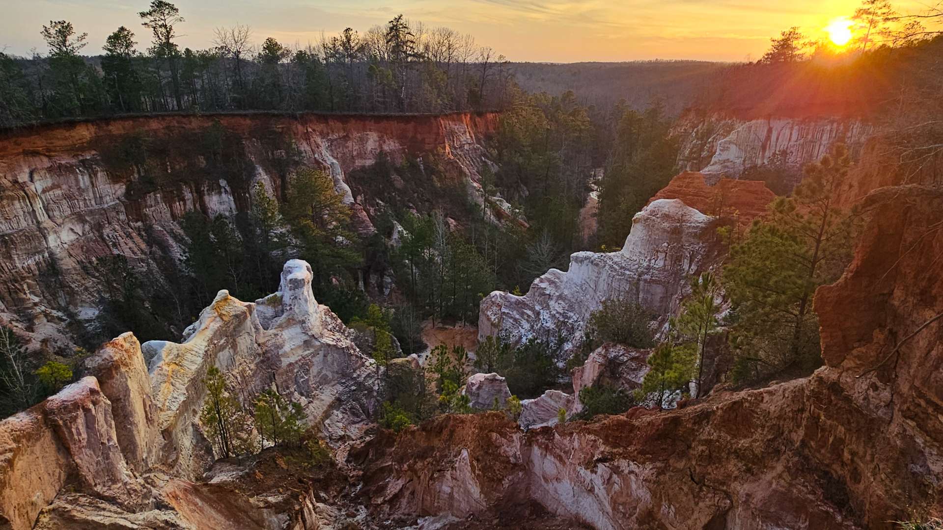 Sunset over colorful canyon cliffs with rugged rock formations and trees in the valley.