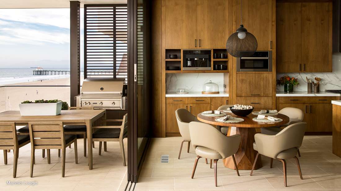 Contemporary living room with large sectional sofa, floor-to-ceiling windows overlooking lush greenery, and sleek entertainment wall with mounted flat-screen TV.