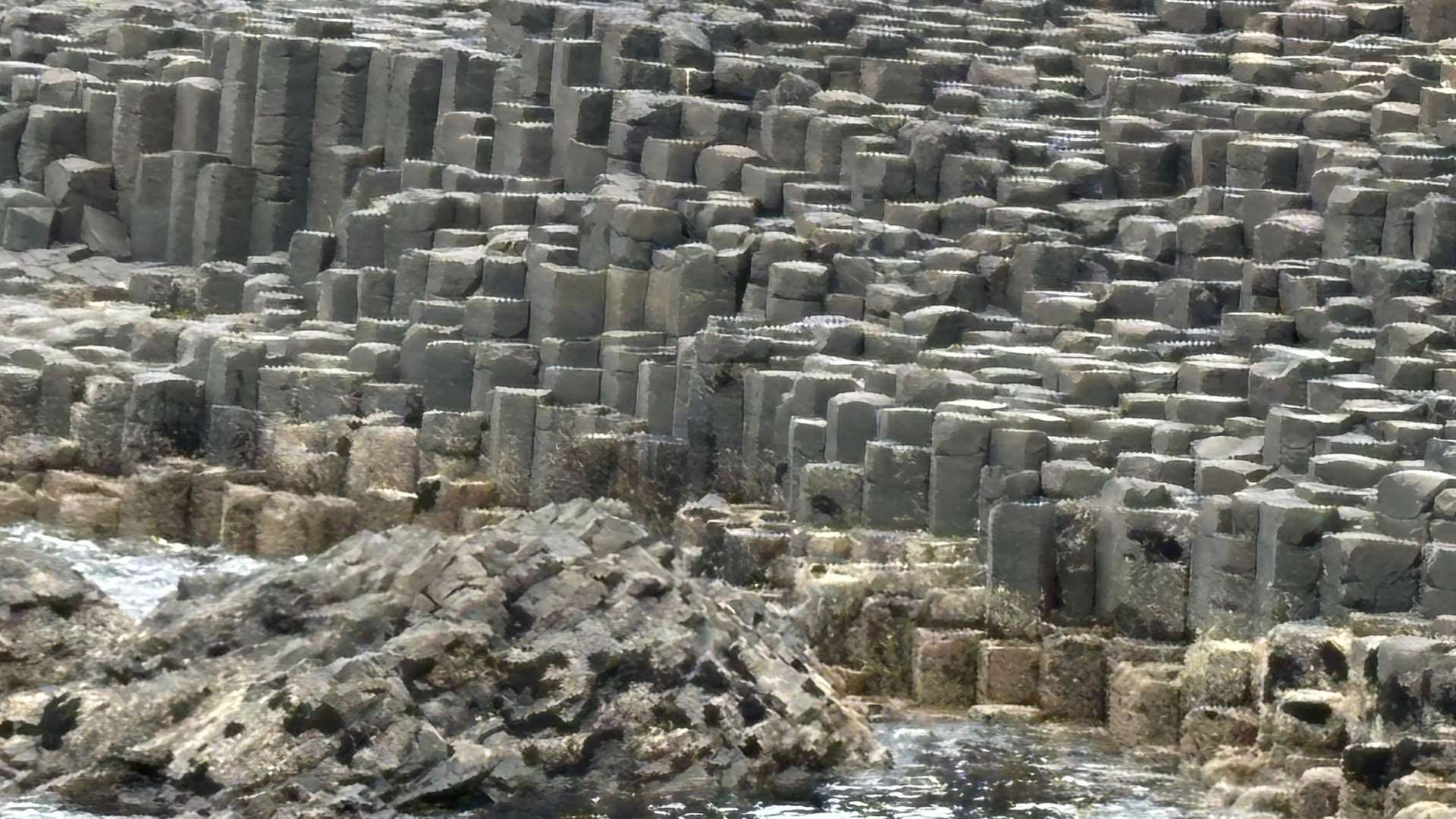 Close-up of interlocking hexagonal basalt columns along rocky shoreline with ocean water at the base.