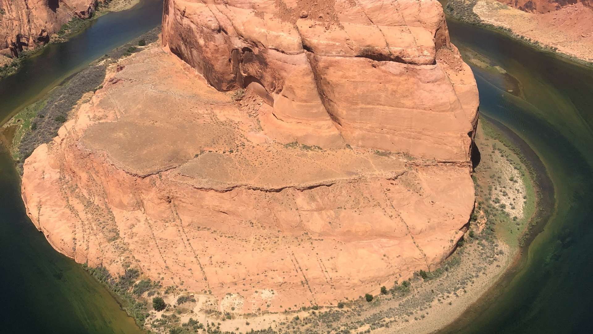 Curved sandstone formation surrounded by green river water in a canyon landscape under bright sunlight.