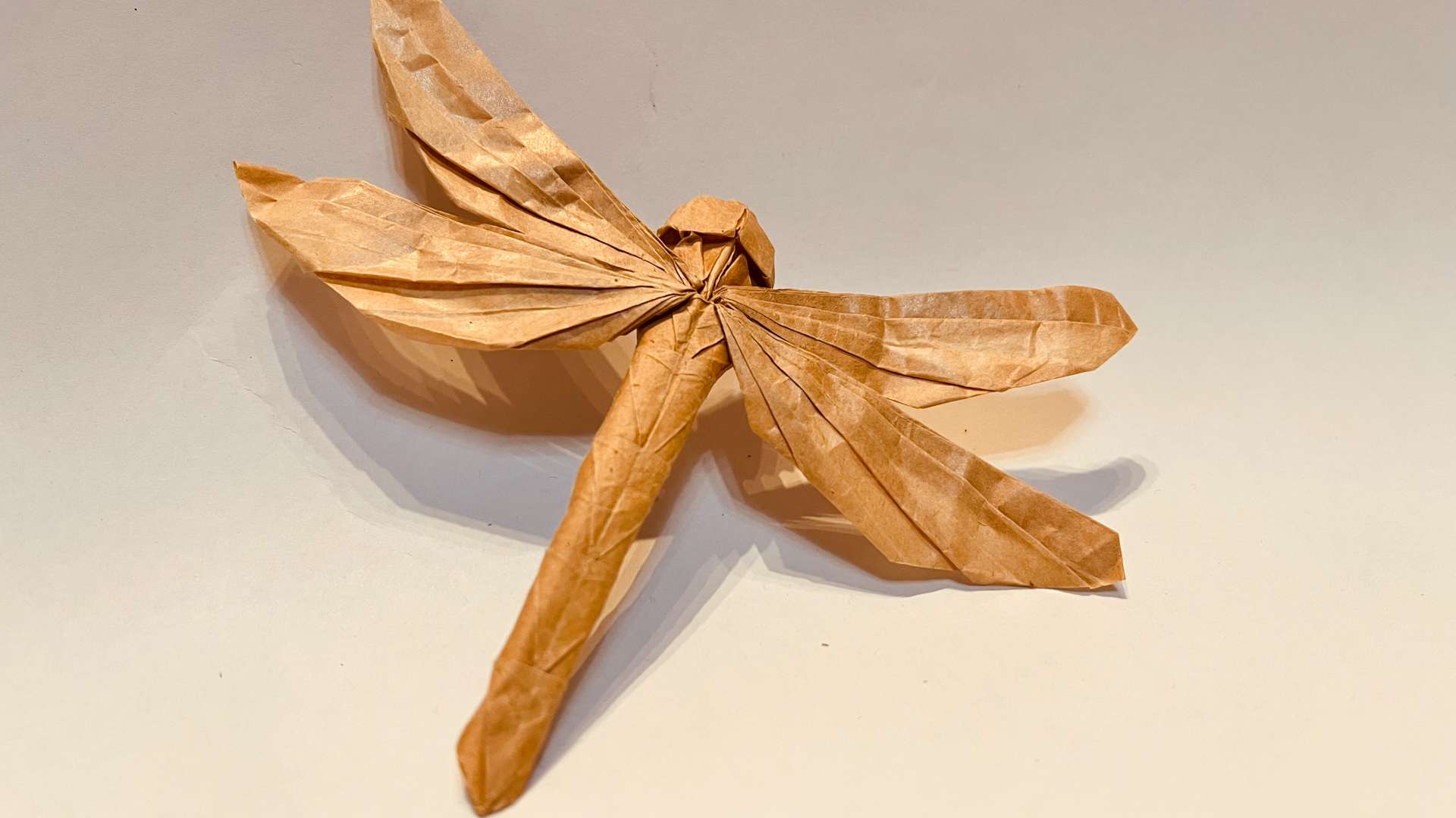   Origami dragonfly crafted from brown paper with detailed folded wings and body on a light background.
