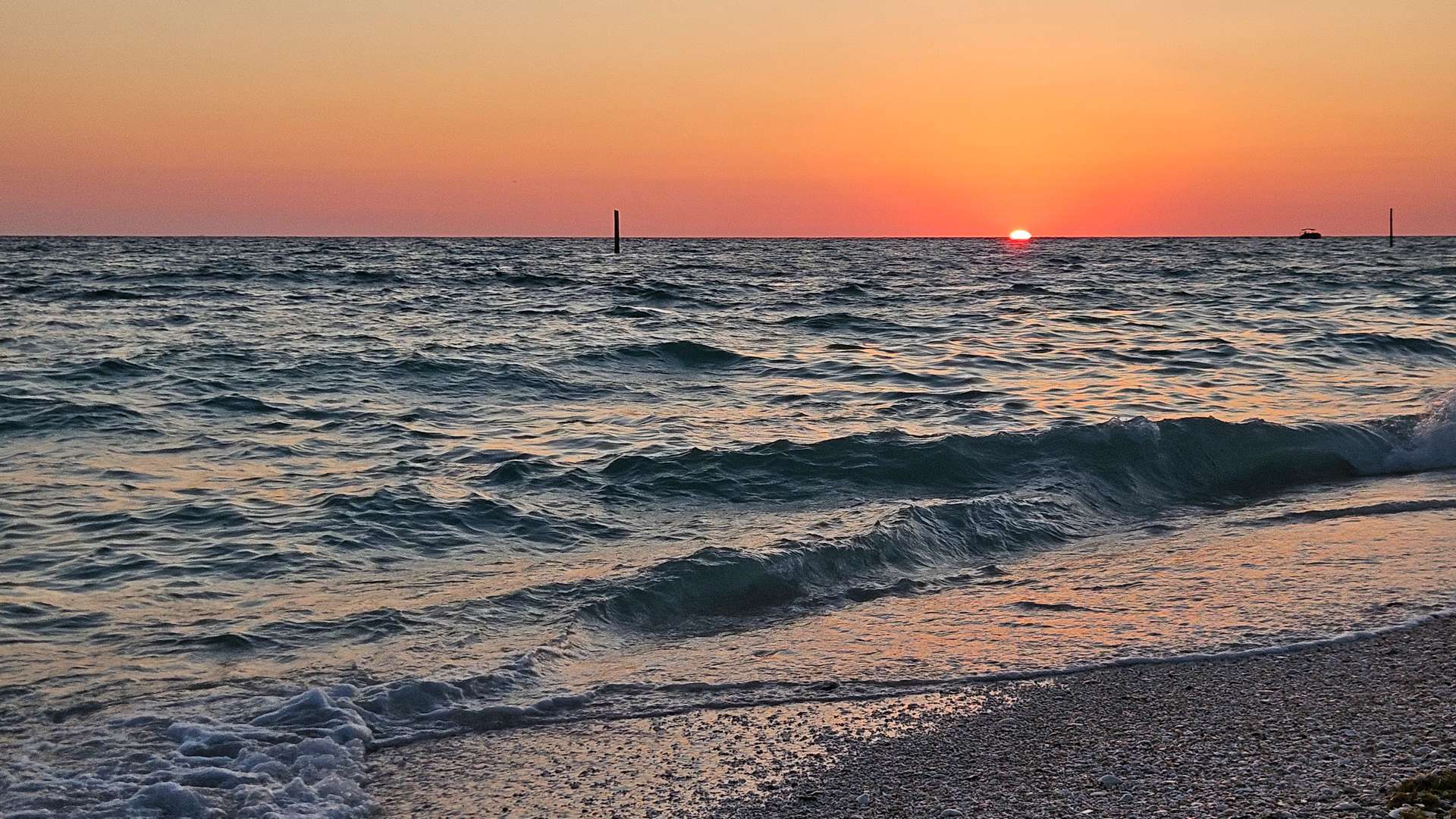 Golden sunset over calm ocean waves with a sandy shoreline in the foreground.