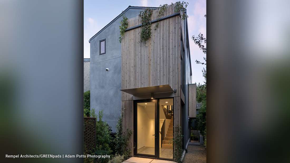 Modern two-story home with vertical wood slat facade, black-framed glass entry door, cantilevered upper section with greenery accents, and minimalist landscaping.