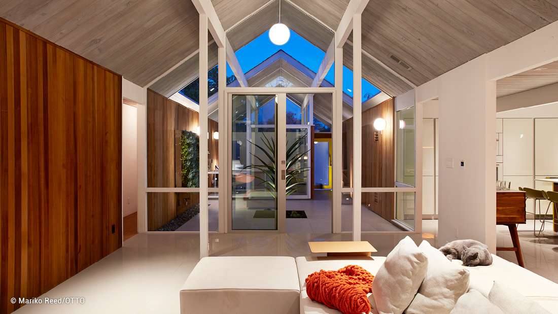 Modern interior with vaulted ceiling, exposed wood panels, glass doors opening to a courtyard, and cozy seating area with neutral tones.