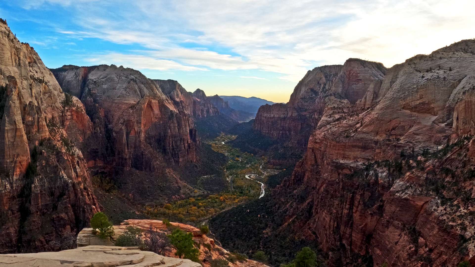   Expansive canyon view with steep red cliffs, winding river below, and a partly cloudy blue sky.