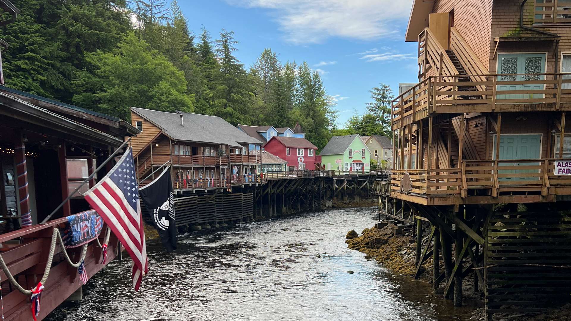 Colorful wooden houses on stilts along a creek in a forested coastal town.