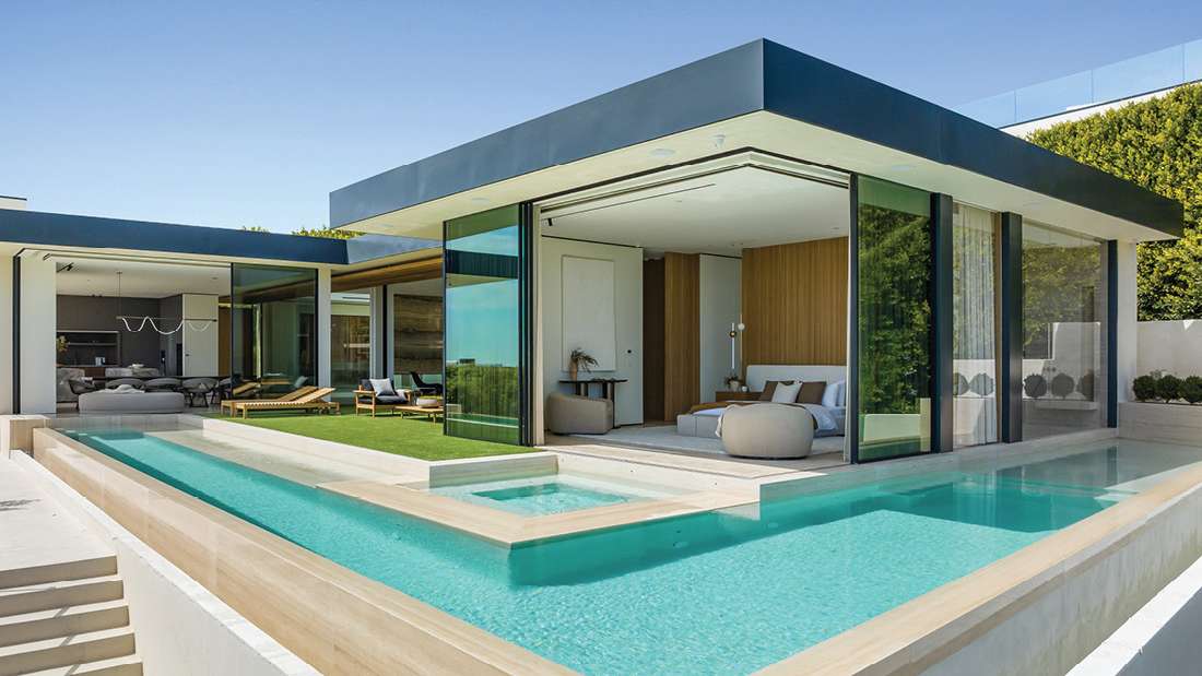 Contemporary luxury home with open-concept design, floor-to-ceiling glass walls, infinity-edge pool, and outdoor lounge area under clear blue sky.