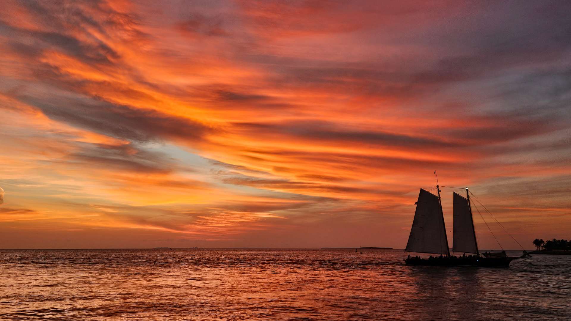 Sailboat silhouetted against vibrant orange and purple sunset over calm ocean waters.
