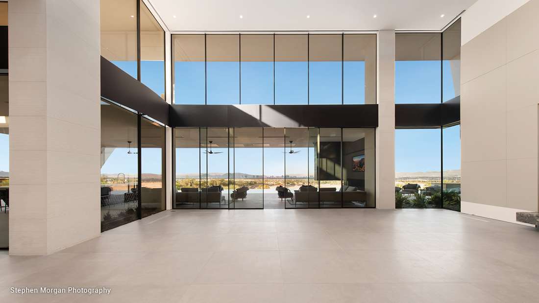 Spacious modern entryway with double-height glass walls, open floor design, and panoramic views of mountains and desert landscape.