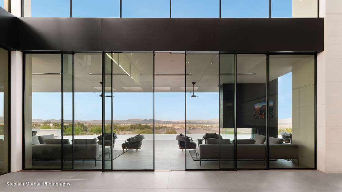 Elegant modern living space with floor-to-ceiling glass doors, open-concept design, and panoramic desert and mountain views.