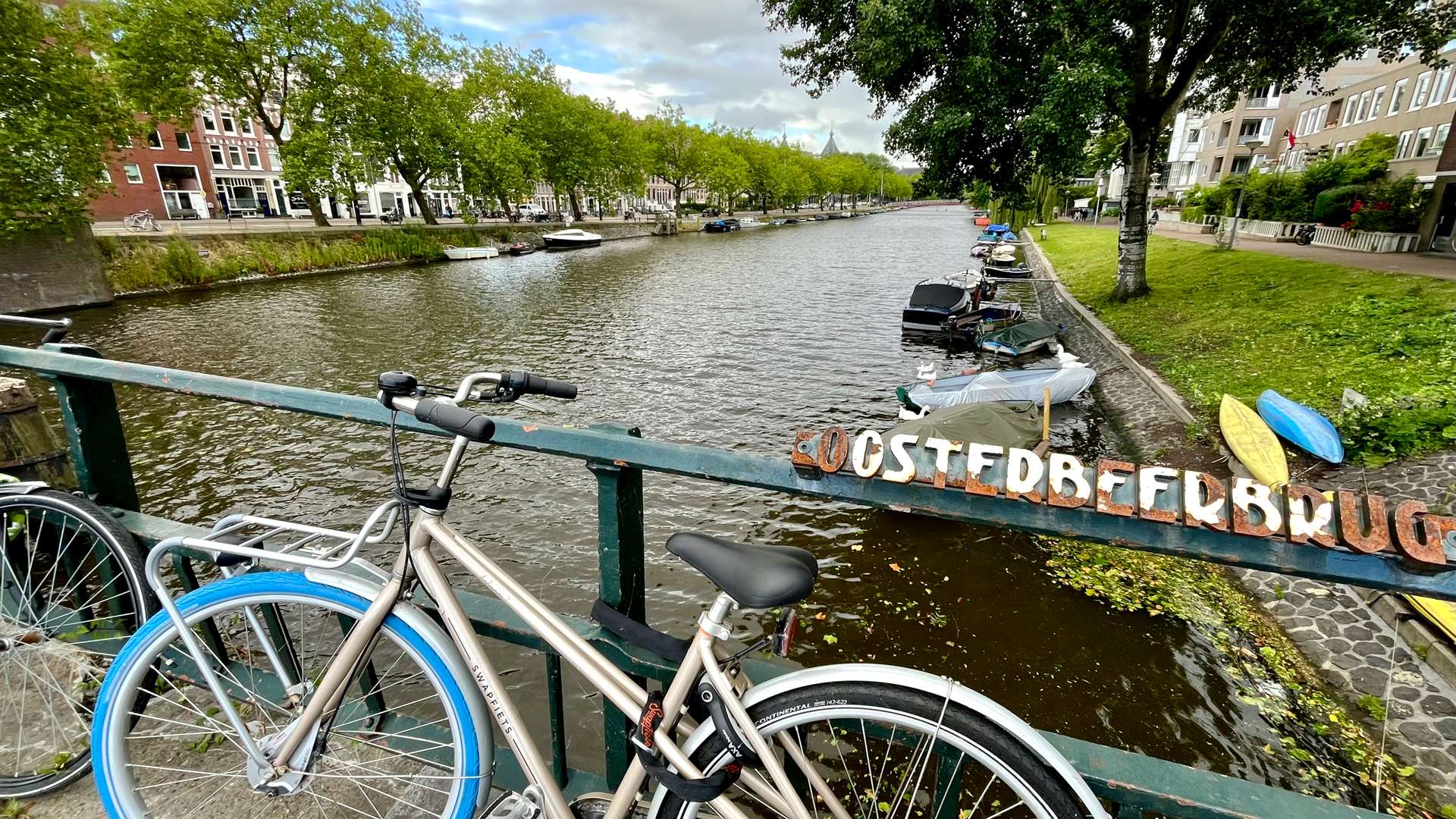 Bicycle parked on a bridge overlooking a canal lined with trees and boats in a European city.