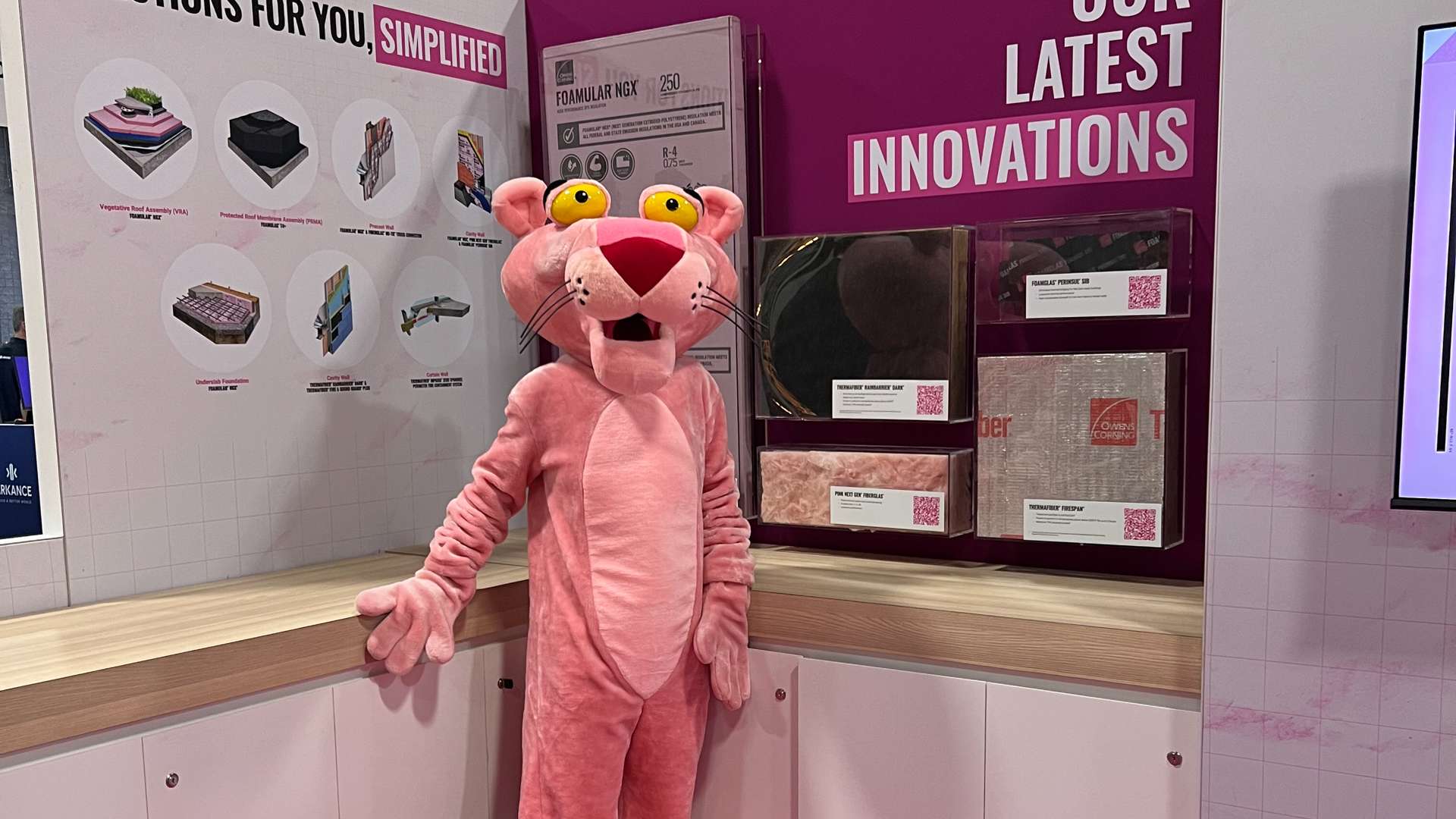 Person in a Pink Panther costume standing at an Owens Corning booth showcasing insulation products and latest innovations.
