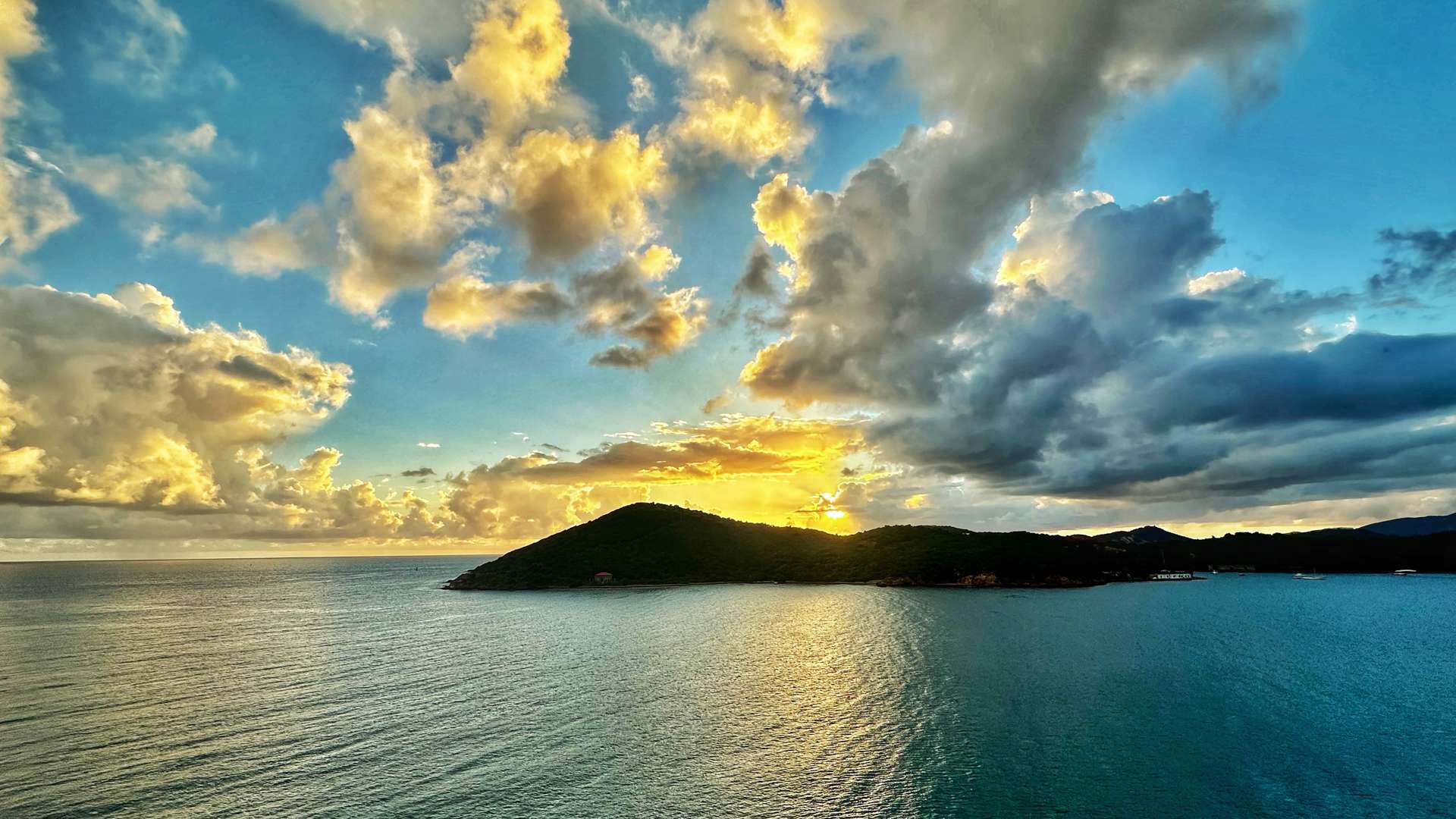   Golden sunset over calm ocean waters with a silhouetted island and dramatic clouds in the sky.