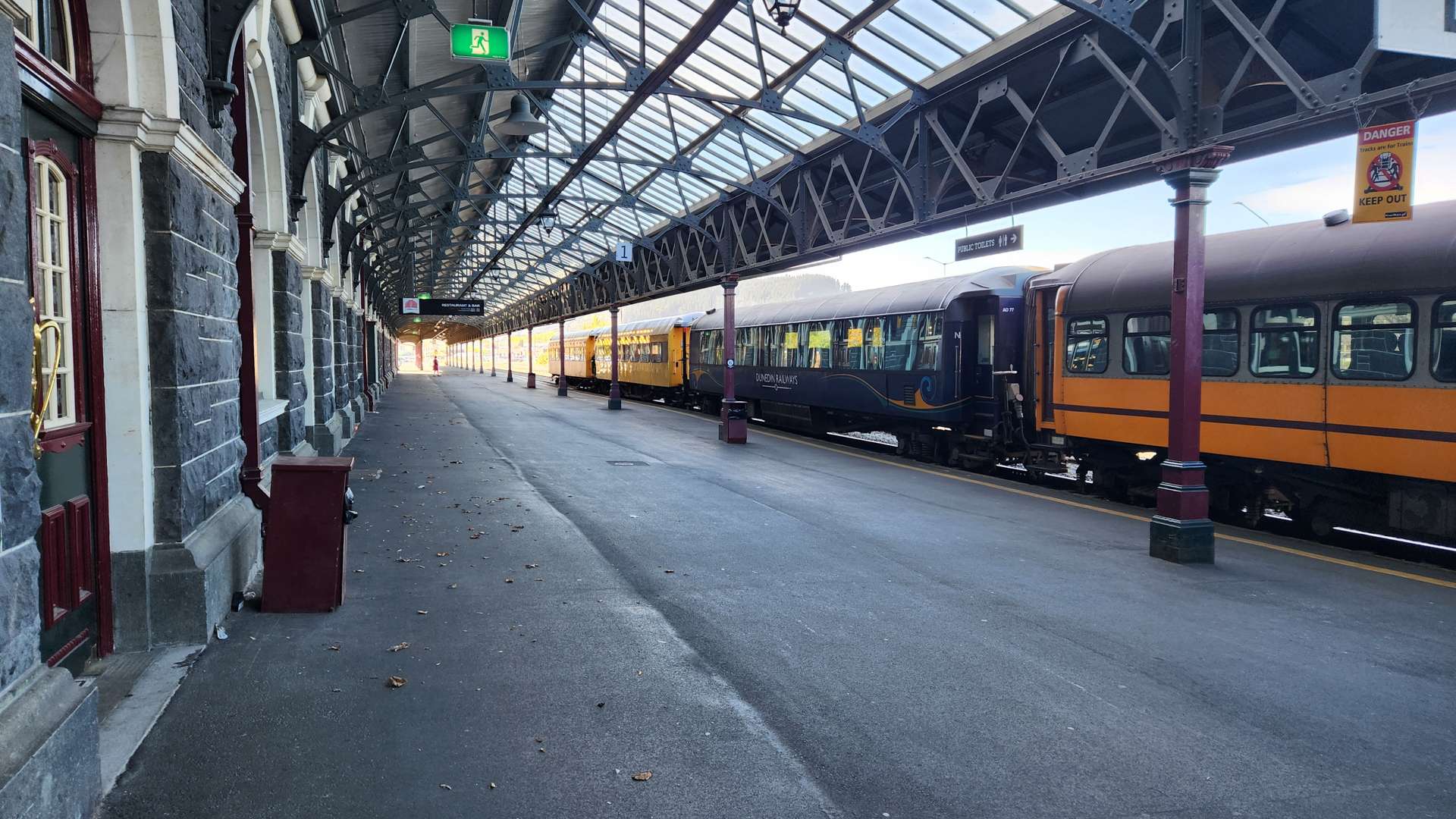   Empty train station platform with vintage-style roof and two parked passenger trains under a glass canopy.