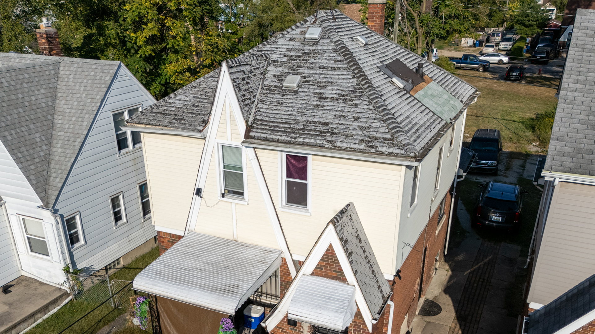 White and tan multistory home with severely damaged roof with extreme granule loss and worn out shingles.