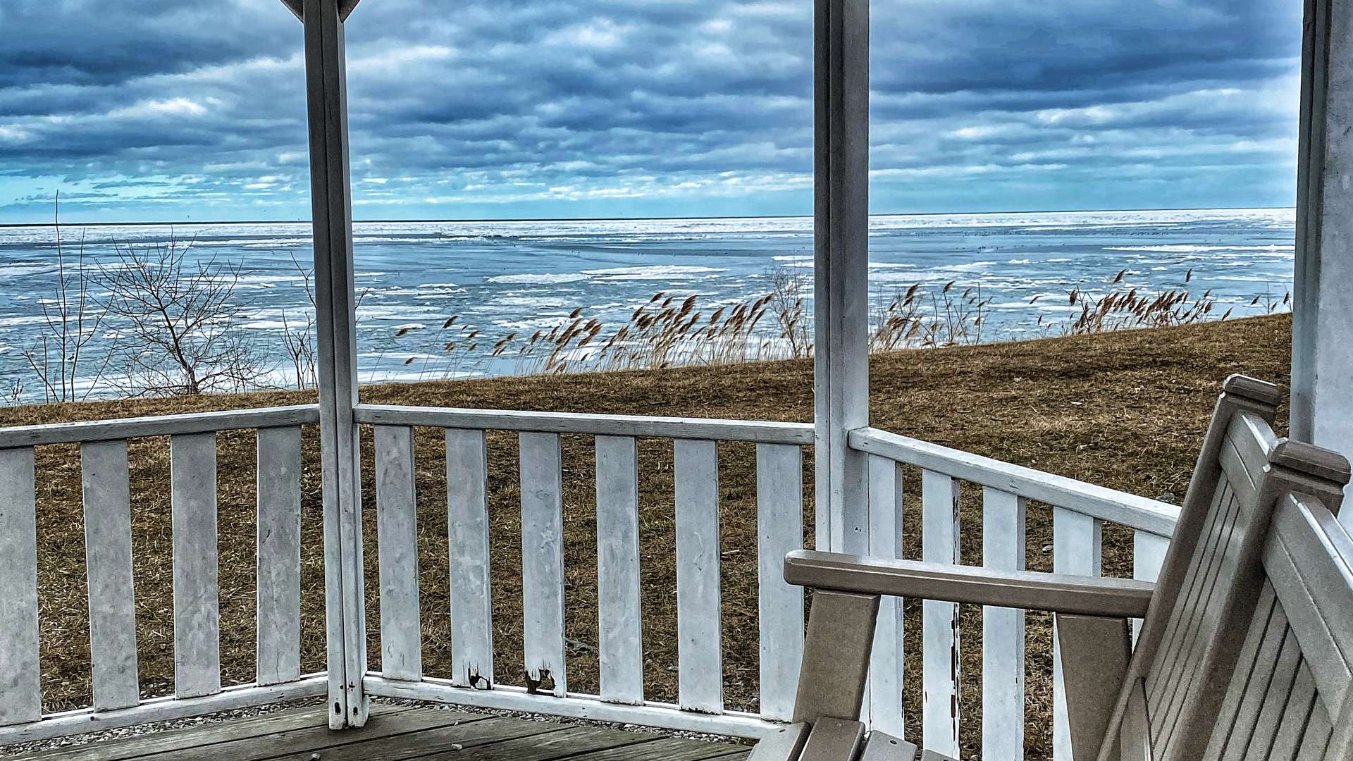   Wooden gazebo overlooking a frozen lake under a cloudy sky with dry grass along the shoreline.