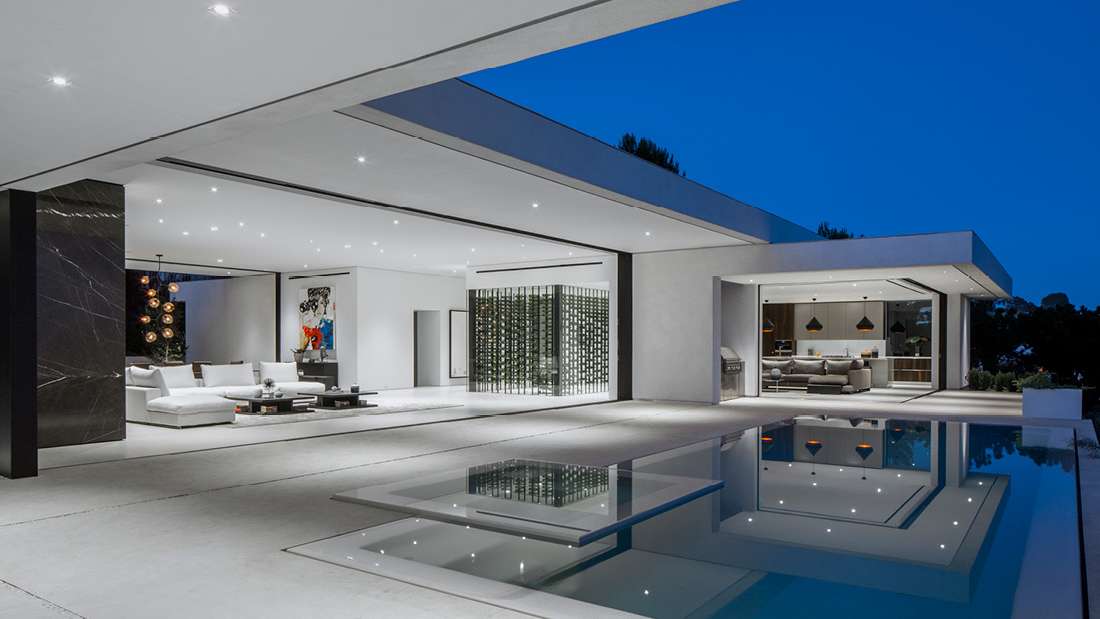 Luxury modern home with open-concept living area, minimalist white interiors, floor-to-ceiling glass walls, and sleek infinity-edge pool reflecting evening lights.