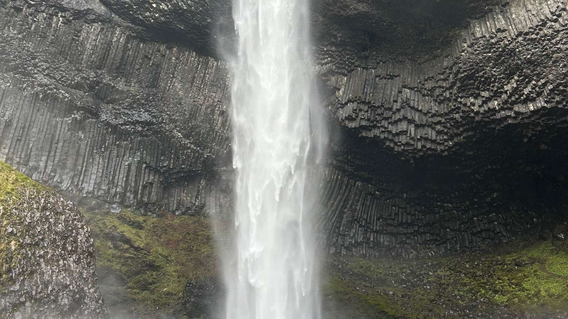   Powerful waterfall plunging over dark basalt rock formations with mist rising from the base.”