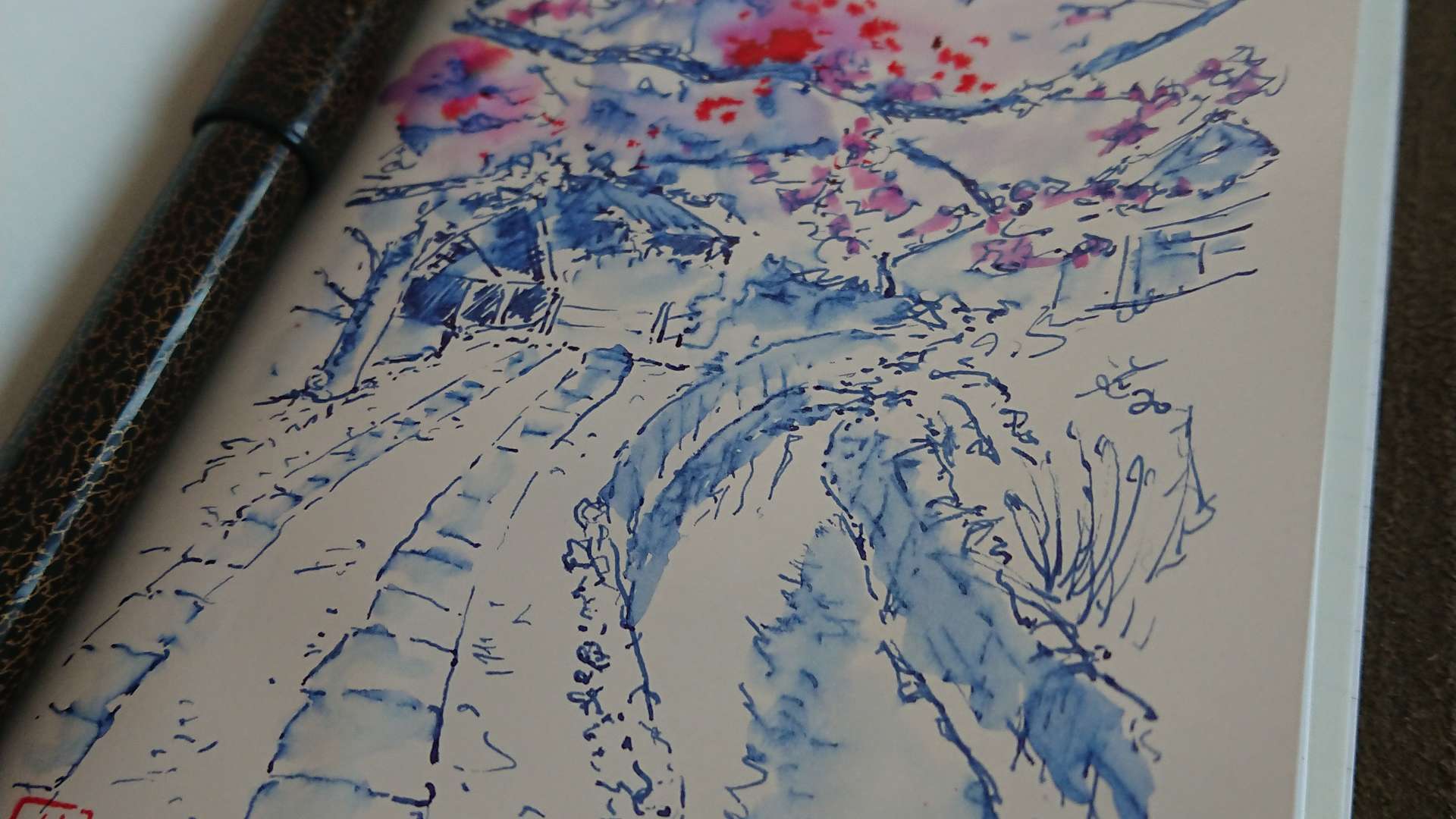   Sketch of a tree-lined path with splashes of pink and purple watercolor, shown in an open notebook with a fountain pen.