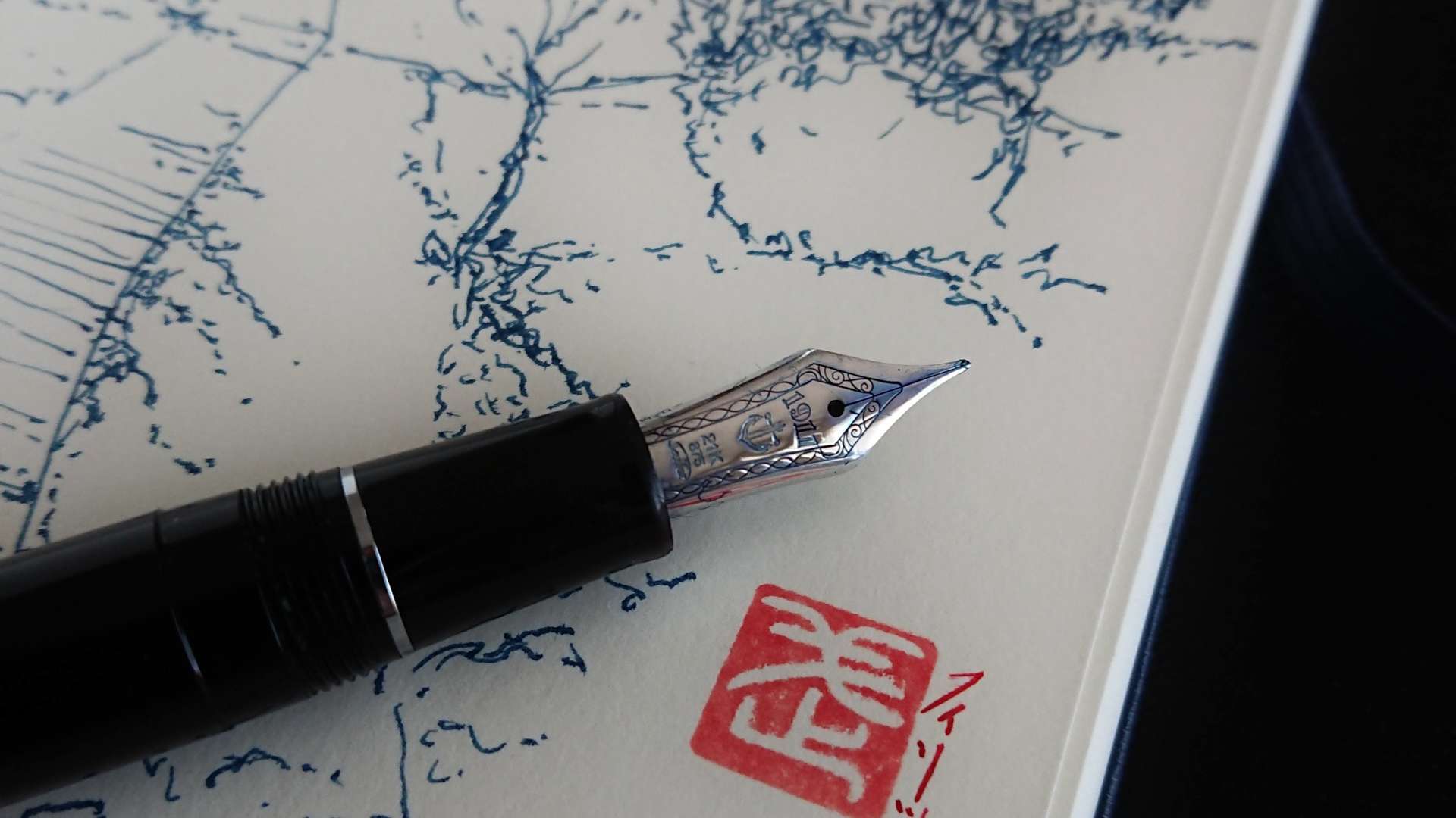   Close-up of a fountain pen resting on a sketch with blue ink lines and a red Japanese-style stamp.