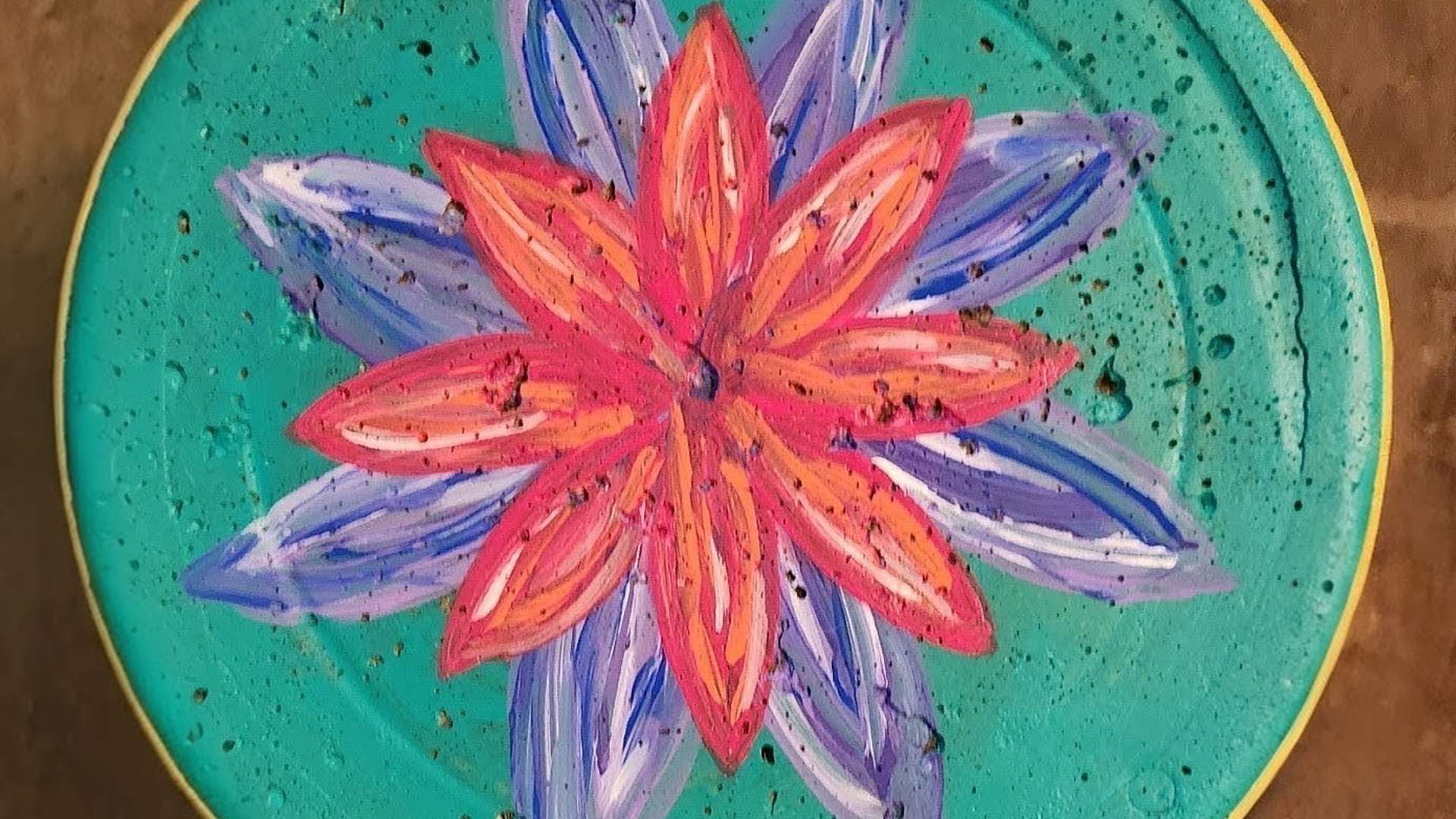  Hand-painted mandala-style flower with red and purple petals on a turquoise circular surface.