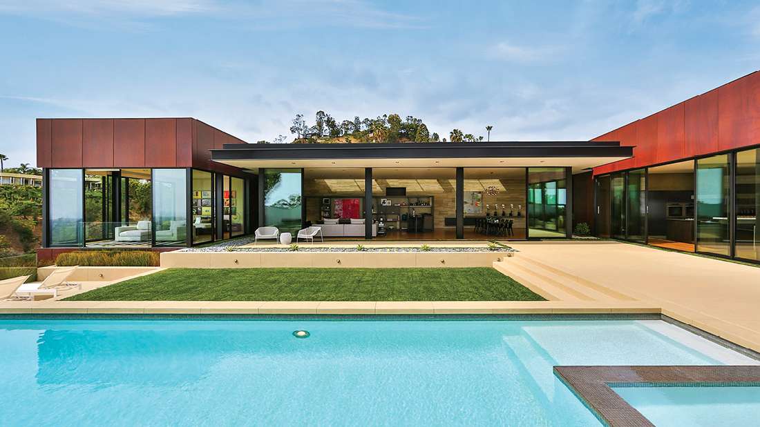 Contemporary single-story luxury home with rust-colored metal panels, floor-to-ceiling glass walls, flat roof design, and outdoor swimming pool with integrated spa.
