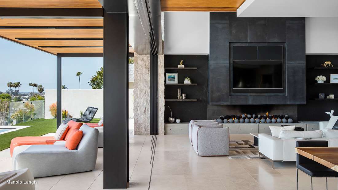 Contemporary open-concept living space with sleek black fireplace wall, built-in shelving, modern lounge chairs, and sliding glass doors opening to a poolside patio.