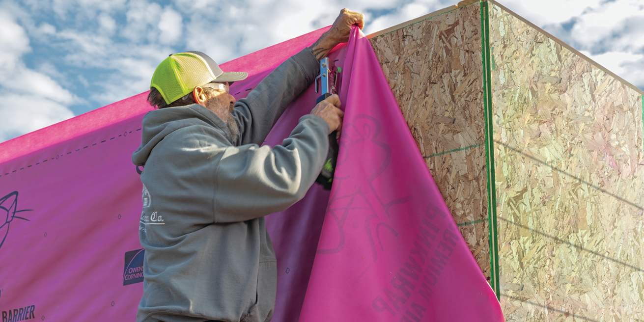 Contractor wearing a yellow ball cap stapling PINKWRAP® Premium air barrier to exterior structure.
