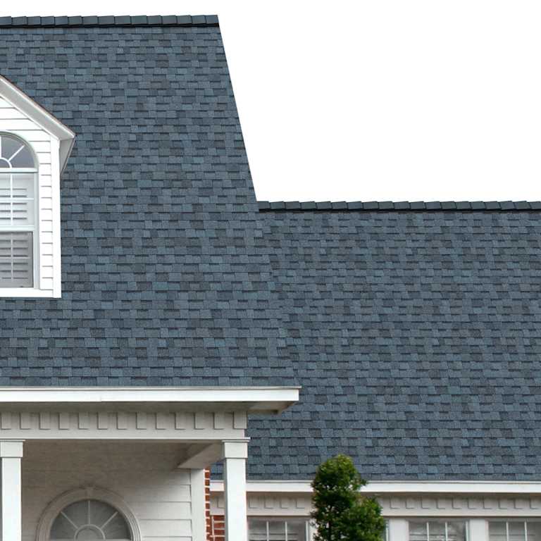 The porch entryway to a home depicts how well Harbor Blue TruDefinition® Duration® light blue, dark blue, and black shingles pair with the white horizontal paneling and a woodgrain door with white columns.