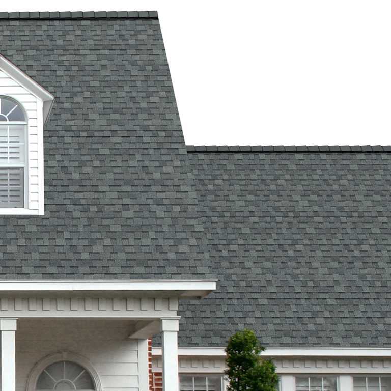 The porch entryway to a home depicts how well Estate Gray Oakridge® greenish-gray shingles pair with the white horizontal paneling and a woodgrain door with white columns.
