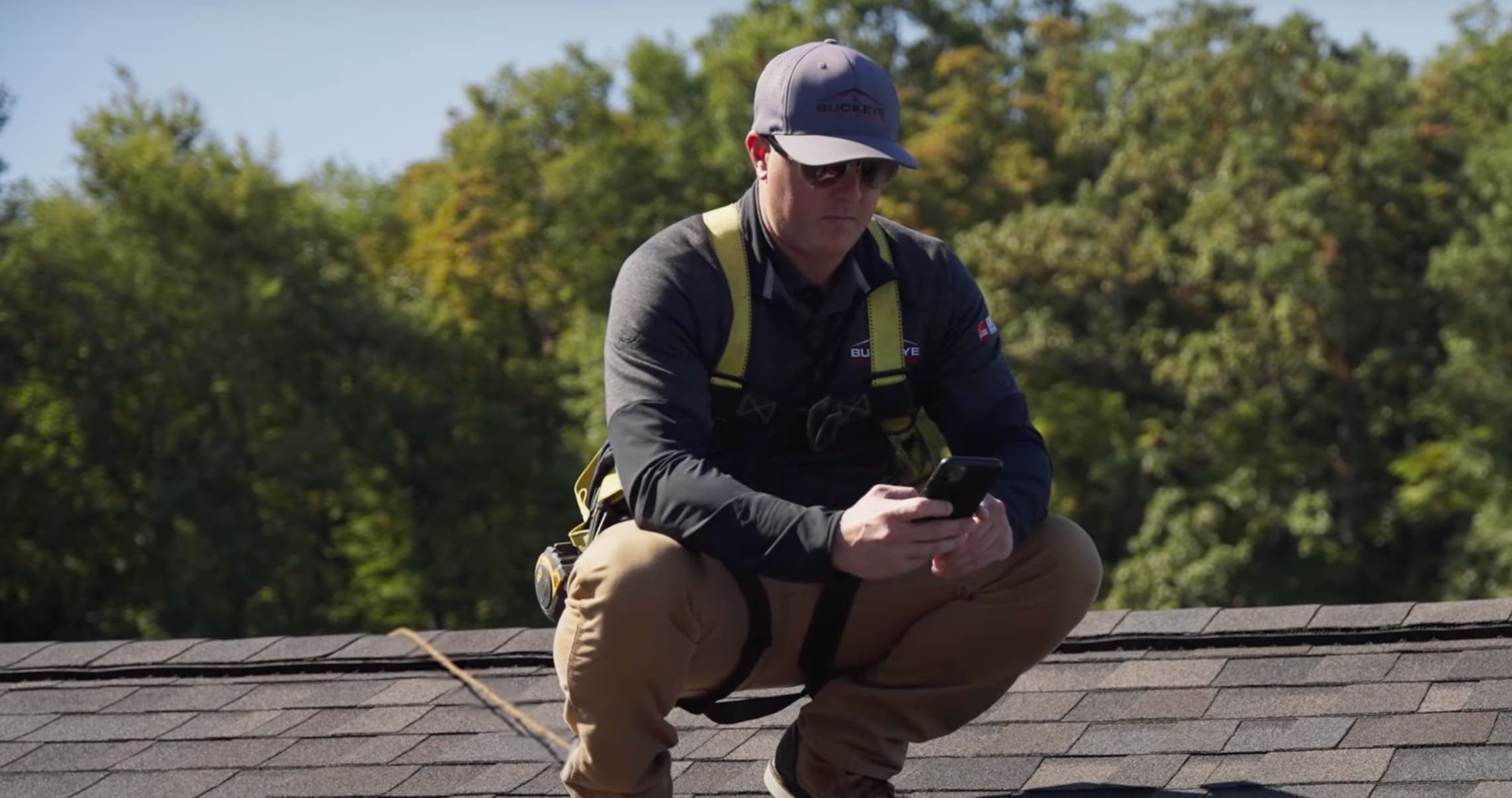 Roofing Contractor squatted down on a roof top taking a picture of the roof ridge with his phone