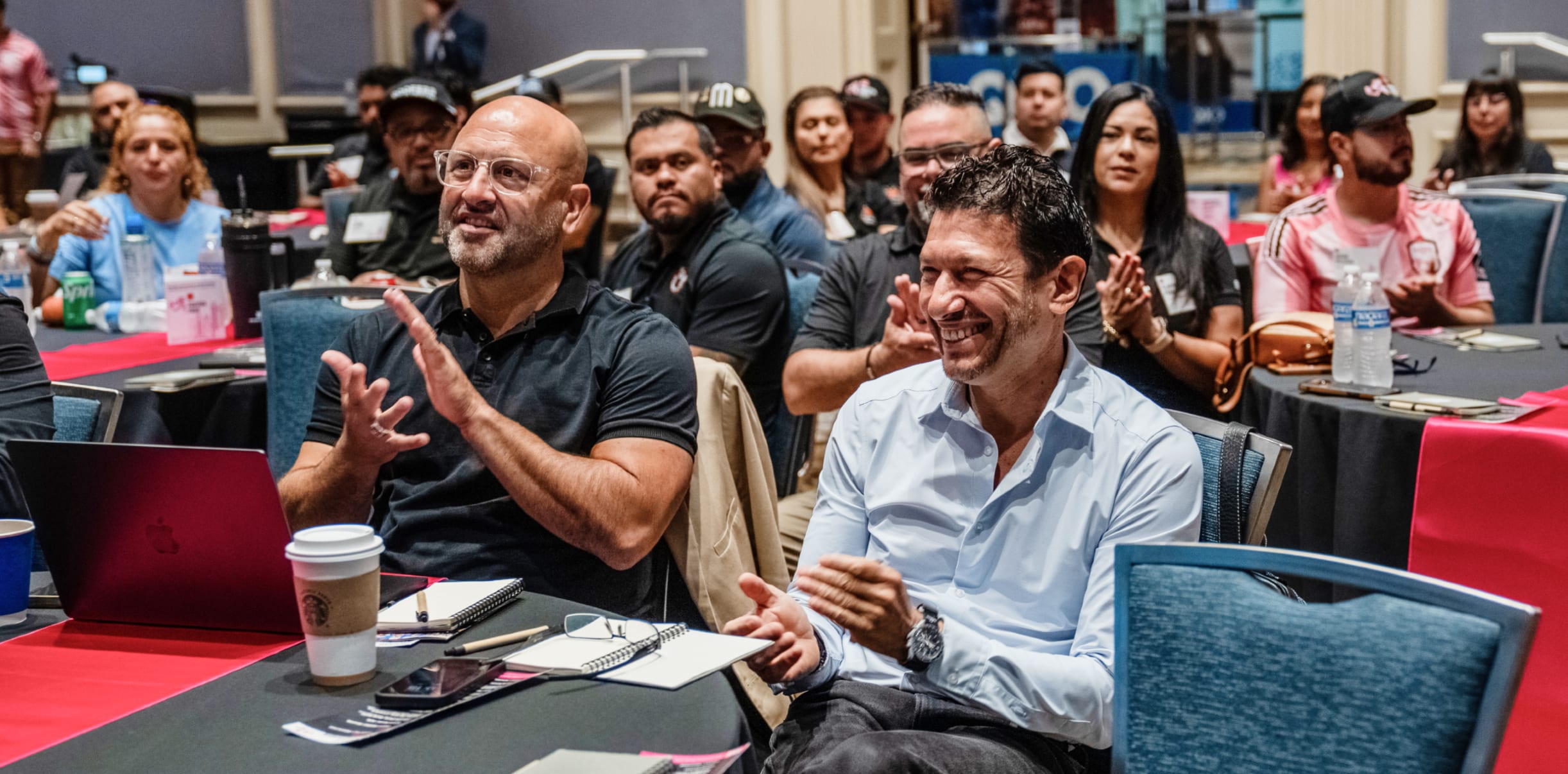 two mens sitting in a conference smiling and clapping